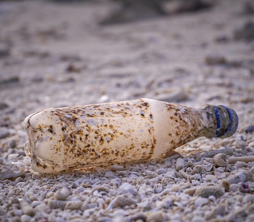 Botella de plástico vacía tirada en la playa entre basura, ilustrando la contaminación ambiental y la necesidad de reciclaje